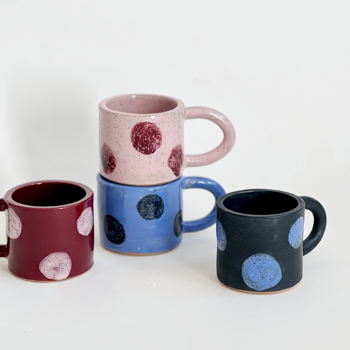 Four ceramic mugs with polka dot patterns on a white background