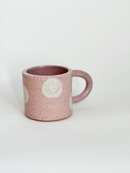 Pink ceramic mug with white speckles and polka dots on a light gray background
